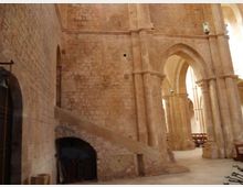 Interno di una chiesa in pietra con grandi archi gotici e pilastri alti, con navate laterali illuminate da luce naturale. In primo piano si vede una rampa in muratura che conduce a un piccolo arco e, sullo sfondo, alcune panche.