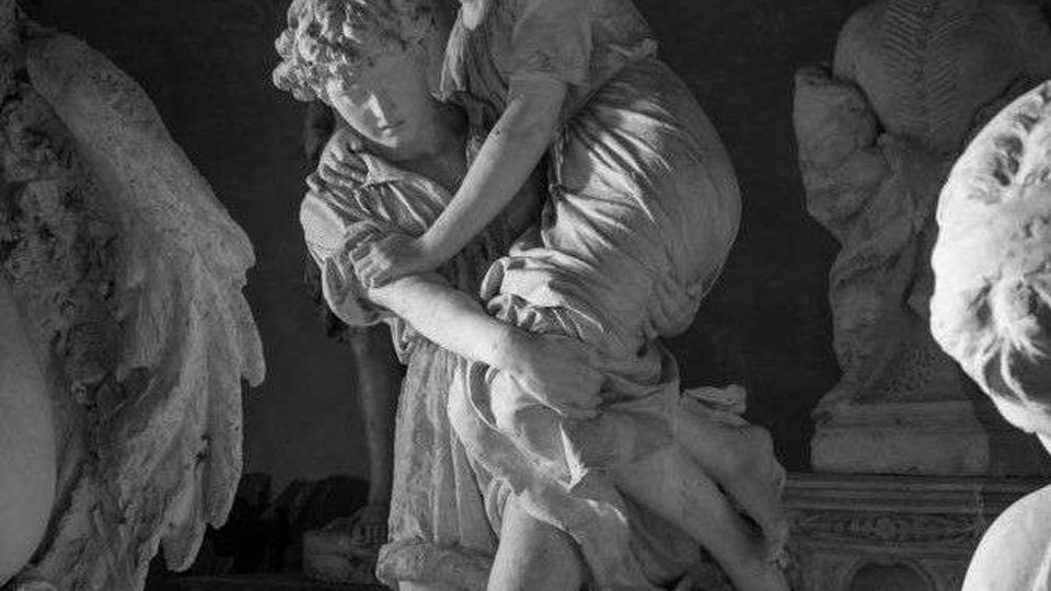 Interno di una galleria o cappella con sculture in marmo: al centro un gruppo statuario raffigurante due figure abbracciate, illuminato lateralmente, con altre statue su piedistalli sullo sfondo e pareti scure a volta.