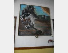 Grande murale dipinto appeso a una parete interna bianca, raffigurante una pantera nera sopra una mappa e macchinari da cantiere, con scritte decorative. Il quadro è incorniciato da una corda e montato sopra una boiserie in legno.