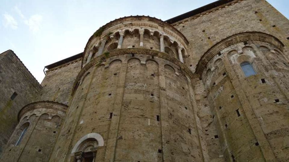 Vista dal basso dell’abside di una chiesa in pietra in stile romanico, con volumi semicircolari e fasce di archetti ciechi. In alto si notano una loggia ad arcate con colonne e piccole finestre inserite nei muri spessi.